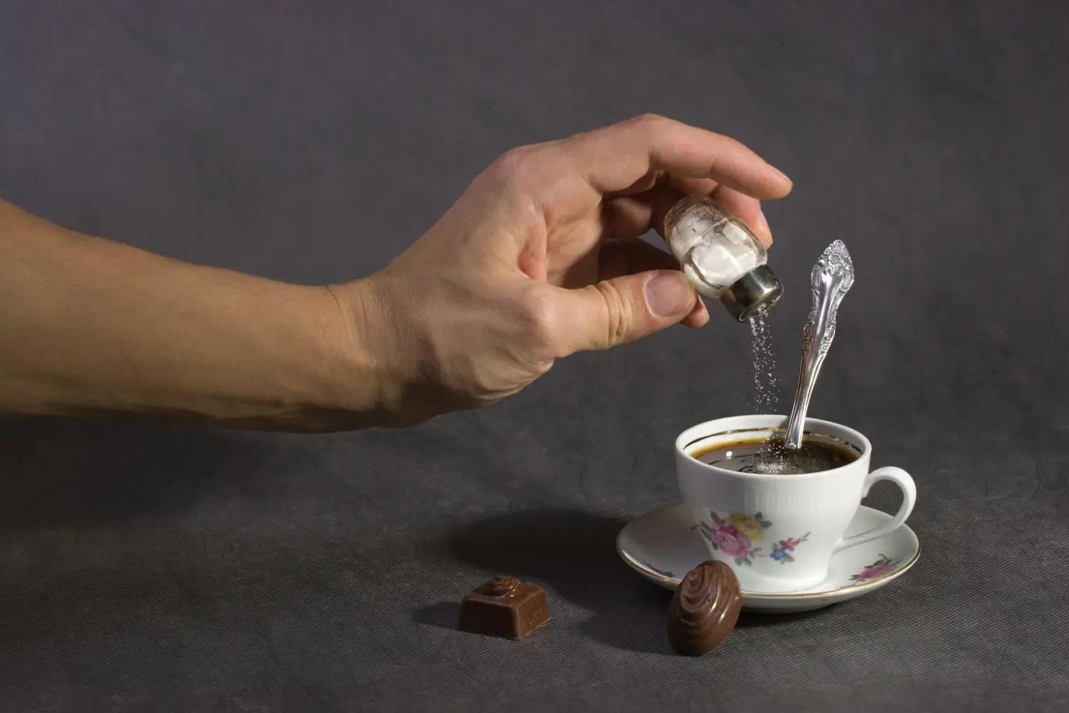 Ruka sype špetku soli do šálku horké kávy vedle kousků čokolády